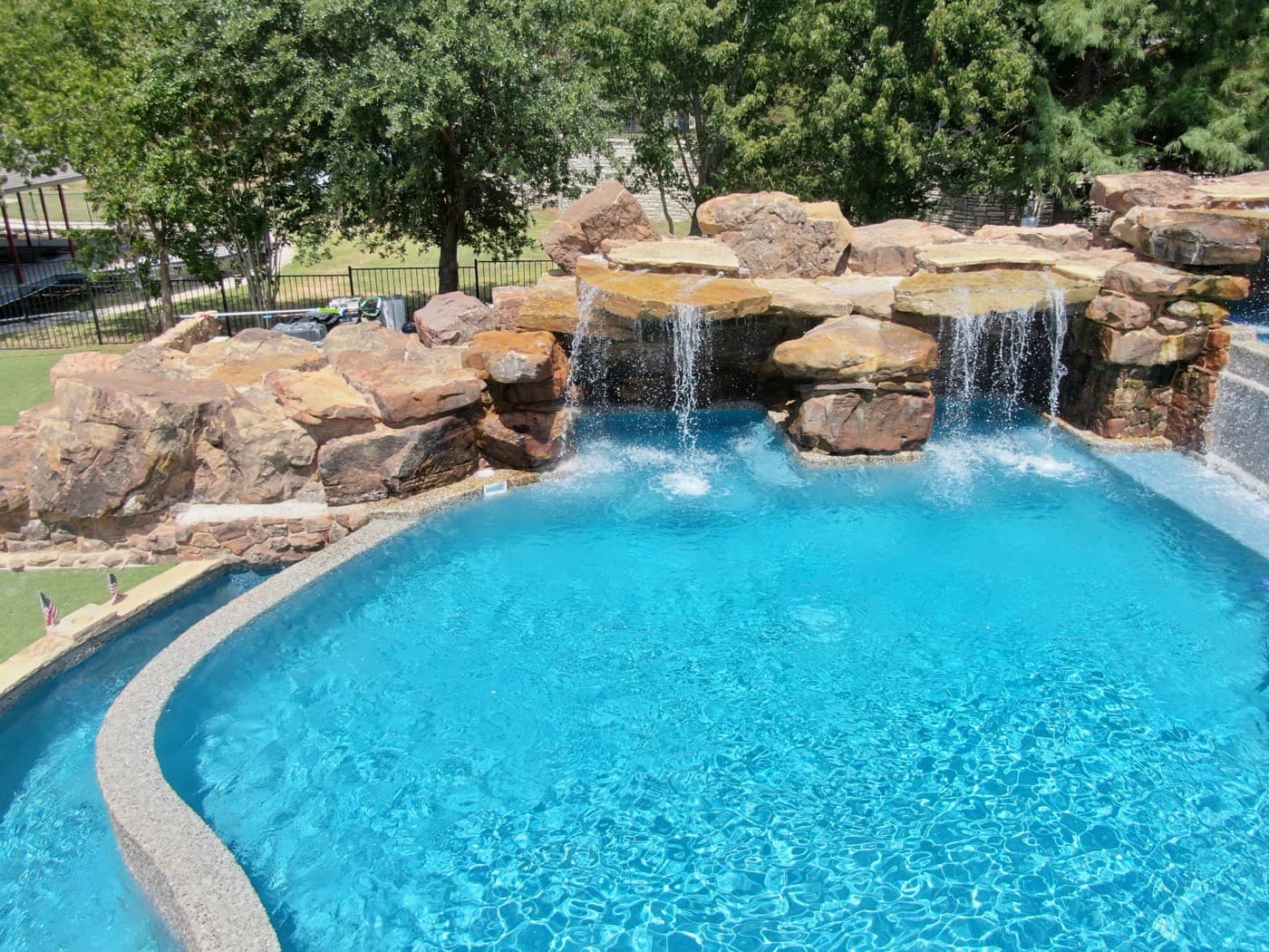 A backyard pool with crystal-clear blue water and a natural rock waterfall feature, maintained by Purple Frog Pools