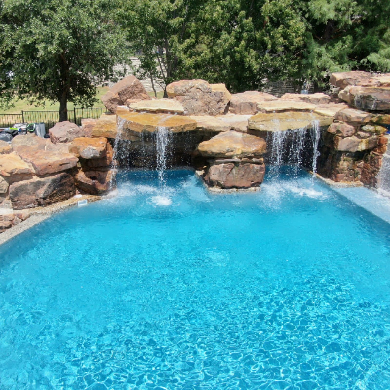 A clear, balanced residential pool with a rock waterfall feature maintained by Purple Frog Pools